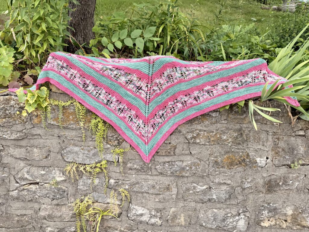 White Branch Shawl in pink, green and variegated yarn displayed on a stone wall