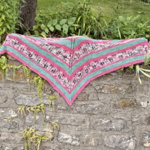 White Branch Shawl in pink, green and variegated yarn displayed on a stone wall